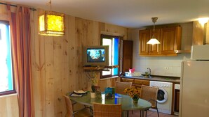Une cuisine avec des murs en bois, une table à manger avec des chaises, un lave-linge et un téléviseur fixé au mur.