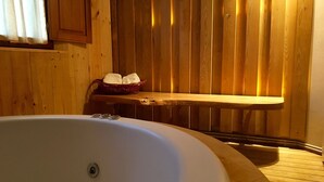 L’intérieur d’un chalet en bois, avec une grande baignoire, un banc en bois et un panier rempli de serviettes.