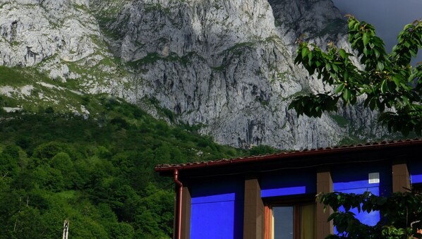 A building with a mountain backdrop, featuring a prominent rocky cliff and lush greenery.