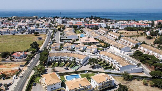 Eine Luftaufnahme einer Küstenwohngegend mit einem markanten weißen Gebäude, das einen Swimmingpool hat, umgeben von kleineren Häusern und freiem Blick auf das Meer.
