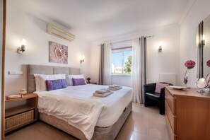 Ein Hotelzimmer mit einem großen Bett, Nachttischen, einem Schminktisch mit Spiegel und einem Fenster mit Vorhängen.