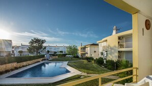Blick auf einen Pool, bewölkter Himmel, ein Gebäude mit Leuchtturm sowie ein Balkon mit Tisch und Buch.