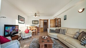 Ein Wohnzimmer mit Fernseher, einer Couch, einem Couchtisch und einem Essbereich mit Stühlen und einem Tisch.