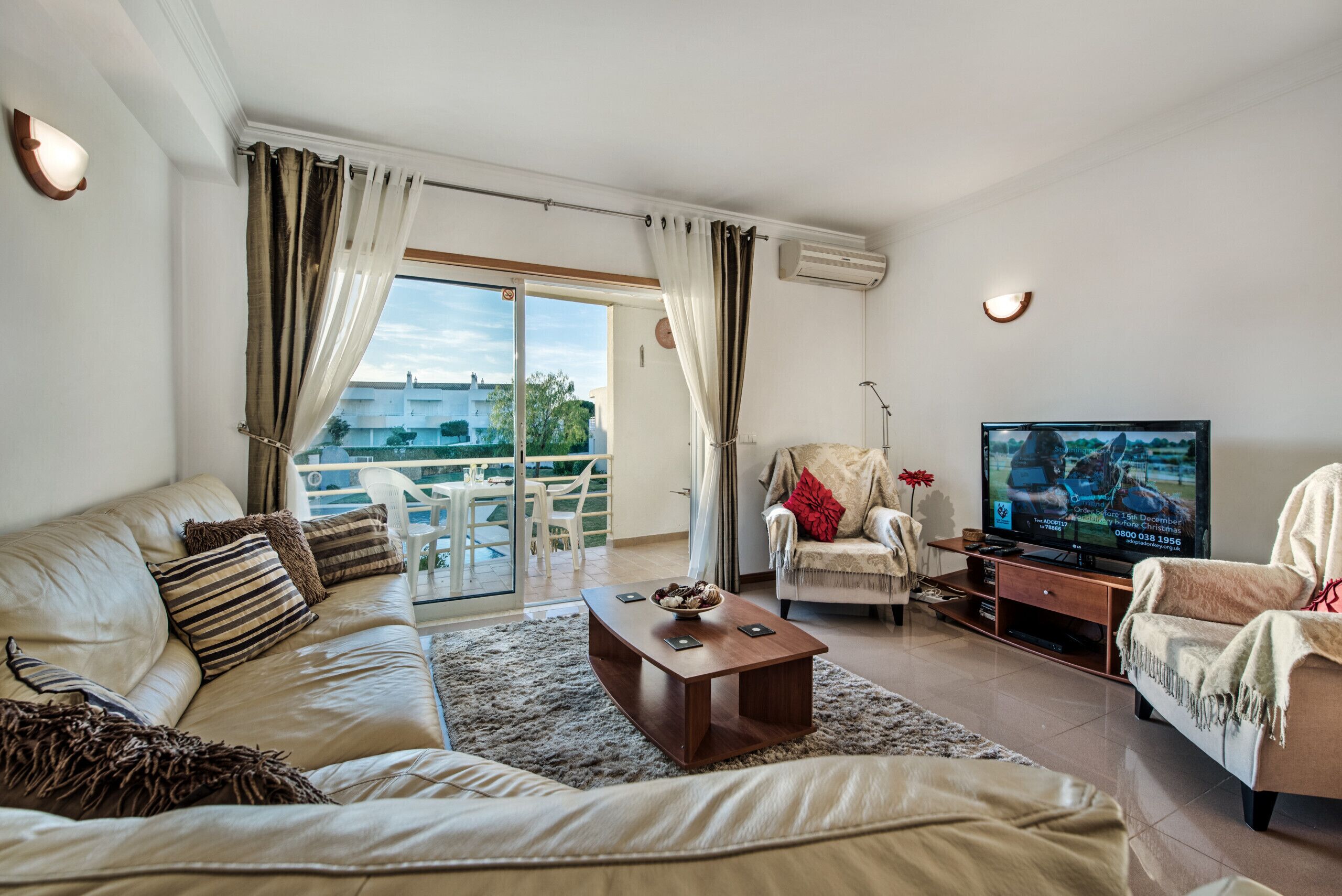 A living room with a sofa, a coffee table, a TV, and a balcony with a view.