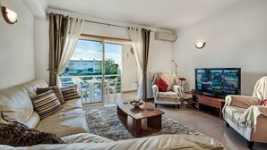 Ein Wohnzimmer mit einer Couch, einem Couchtisch, einem Fernseher und einem Balkon mit Blick.