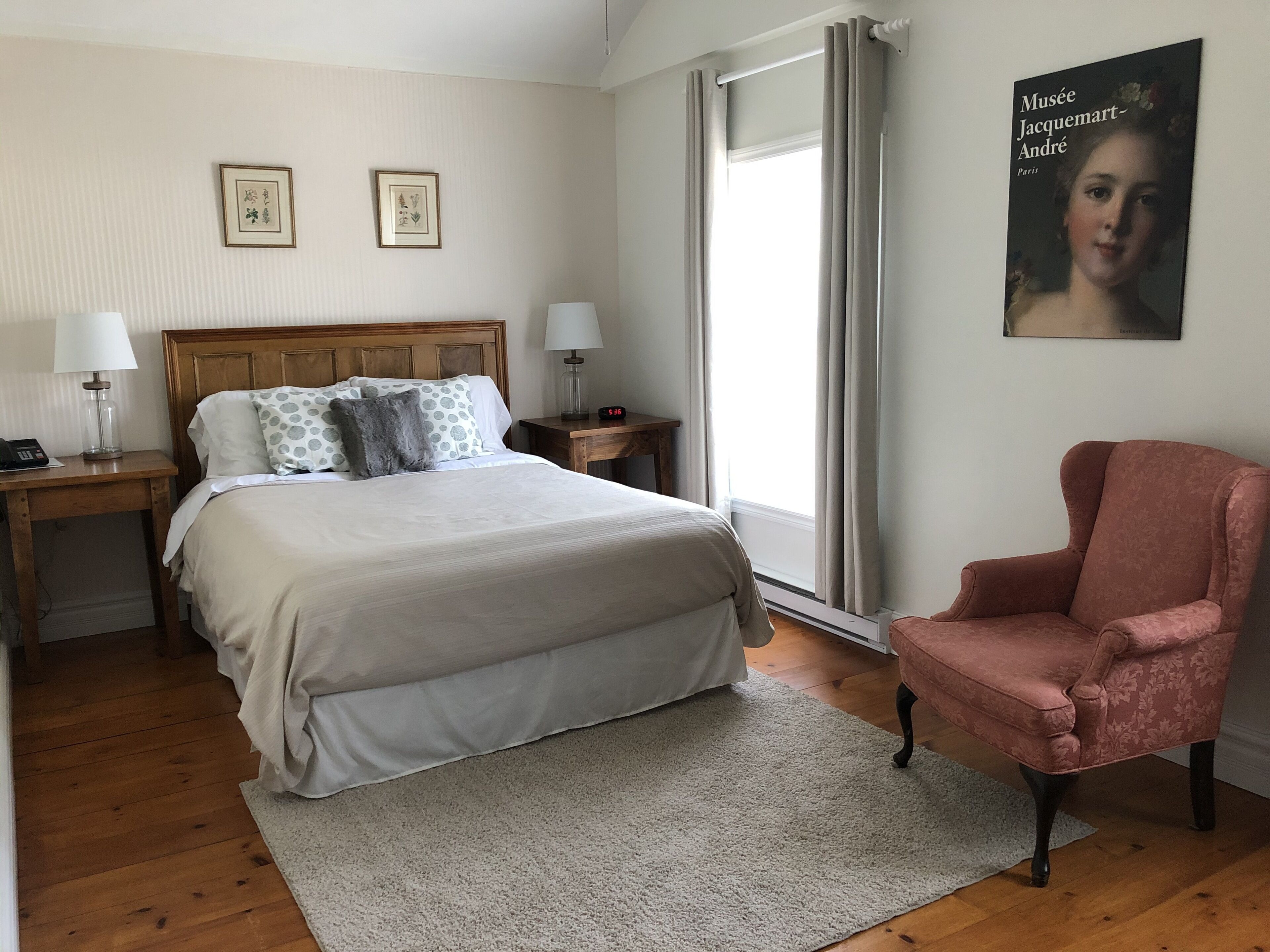 Une chambre à coucher avec un grand lit, deux tables de chevet avec des lampes, une chaise et une affiche accrochée au mur.