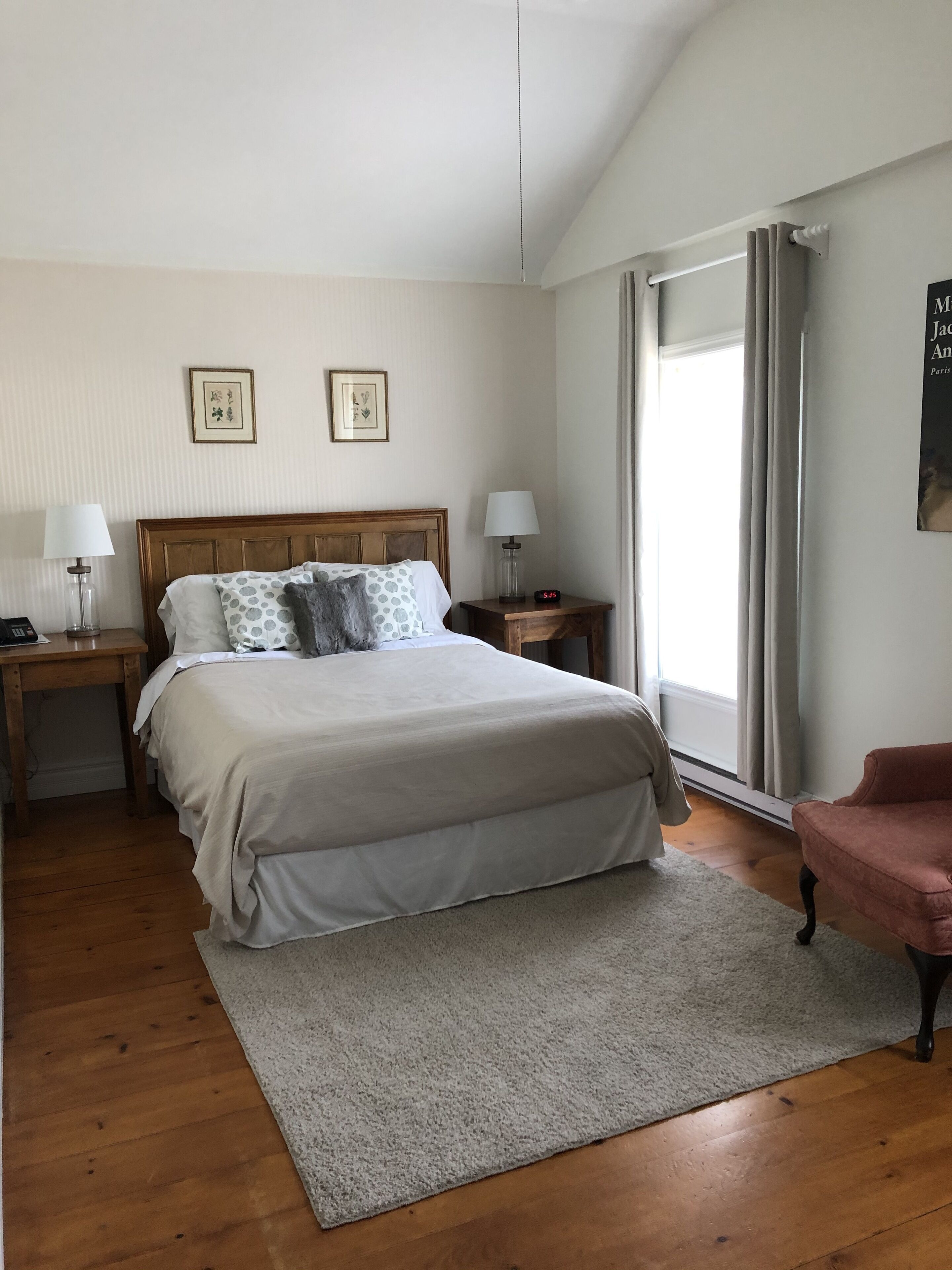 A bedroom with a wooden bed, two bedside tables with lamps, a grey rug, and a pink chair.