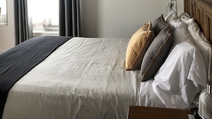 A bedroom with a large bed, a wooden headboard, and three framed pictures on the wall. - Auberge Knowlton (Lac-Brome)