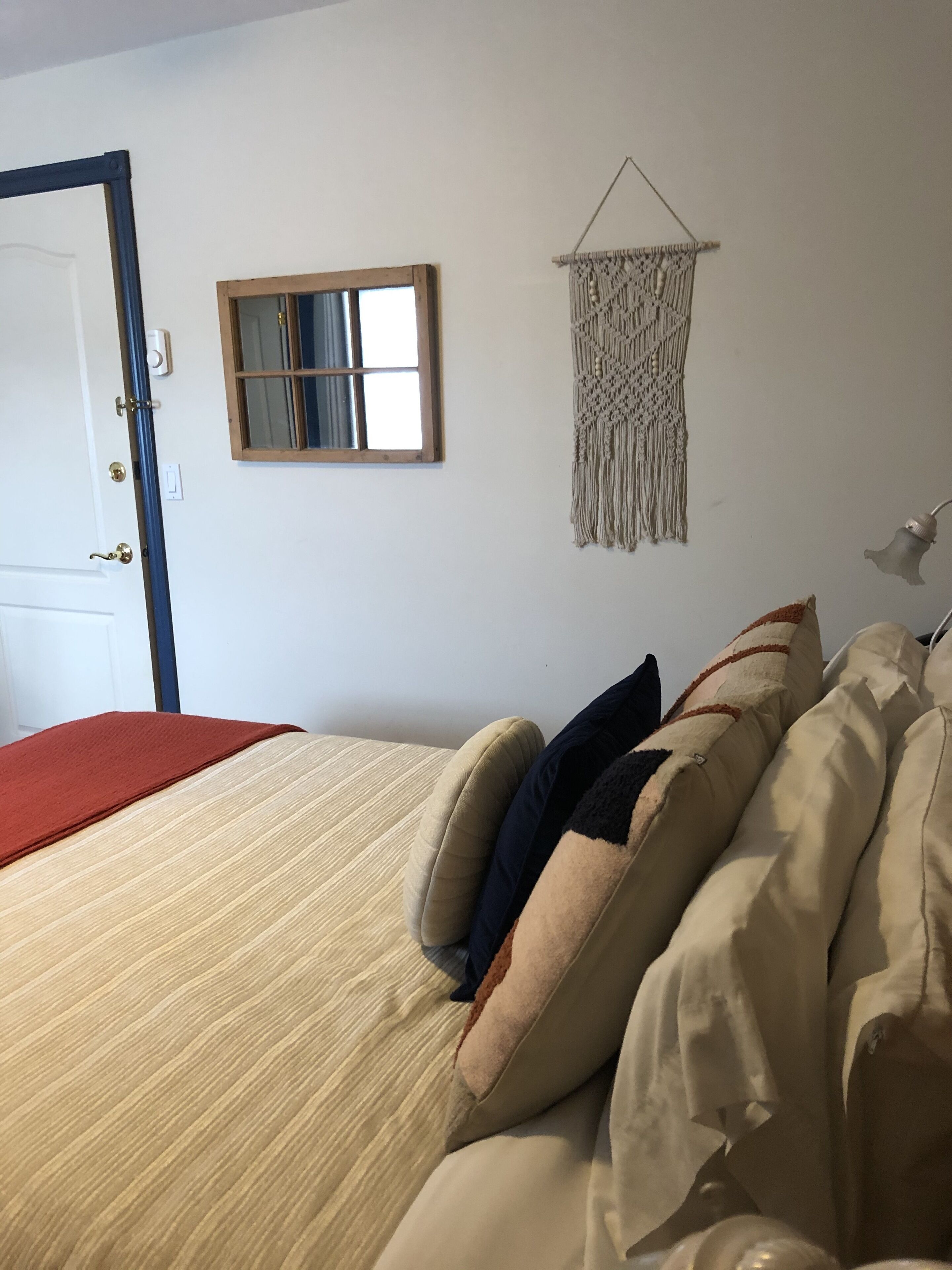 Un lit avec une couverture à rayures, une décoration murale en macramé, un miroir et une porte avec un cadre bleu.