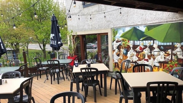 An outdoor patio with tables and chairs, a mural of ducks, and string lights. - Auberge Knowlton (Lac-Brome)
