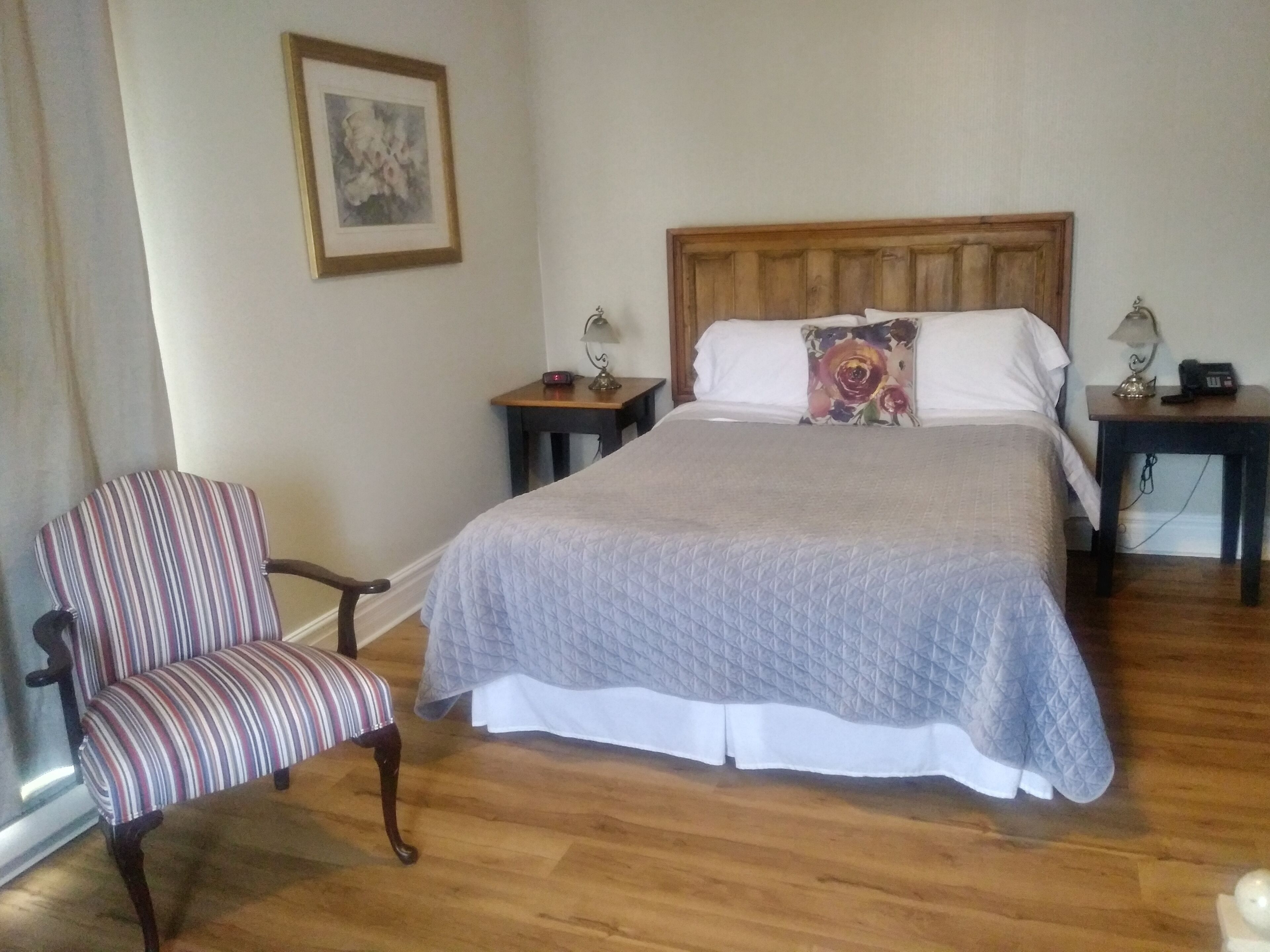 Ein ordentlich eingerichtetes Schlafzimmer mit einem großen Bett, einem gestreiften Sessel und zwei Nachttischen mit Lampen und einem Telefon.