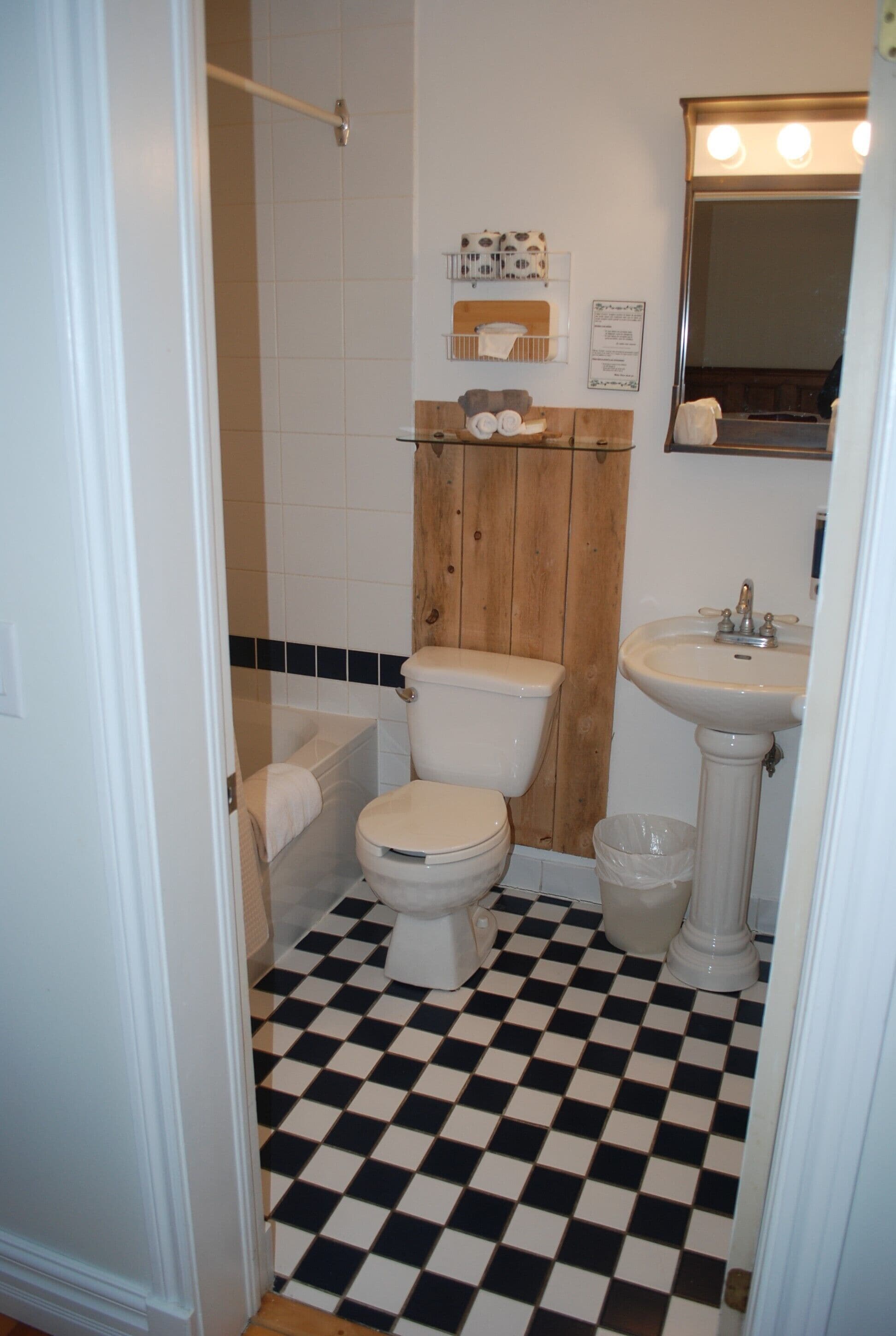 A bathroom with a black and white checkered floor, a toilet, a sink, and a wooden panel above the toilet.