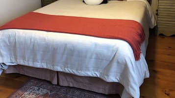 Una cama bien hecha con un edredón rojo, un tapete estampado y un cabecero de madera.
