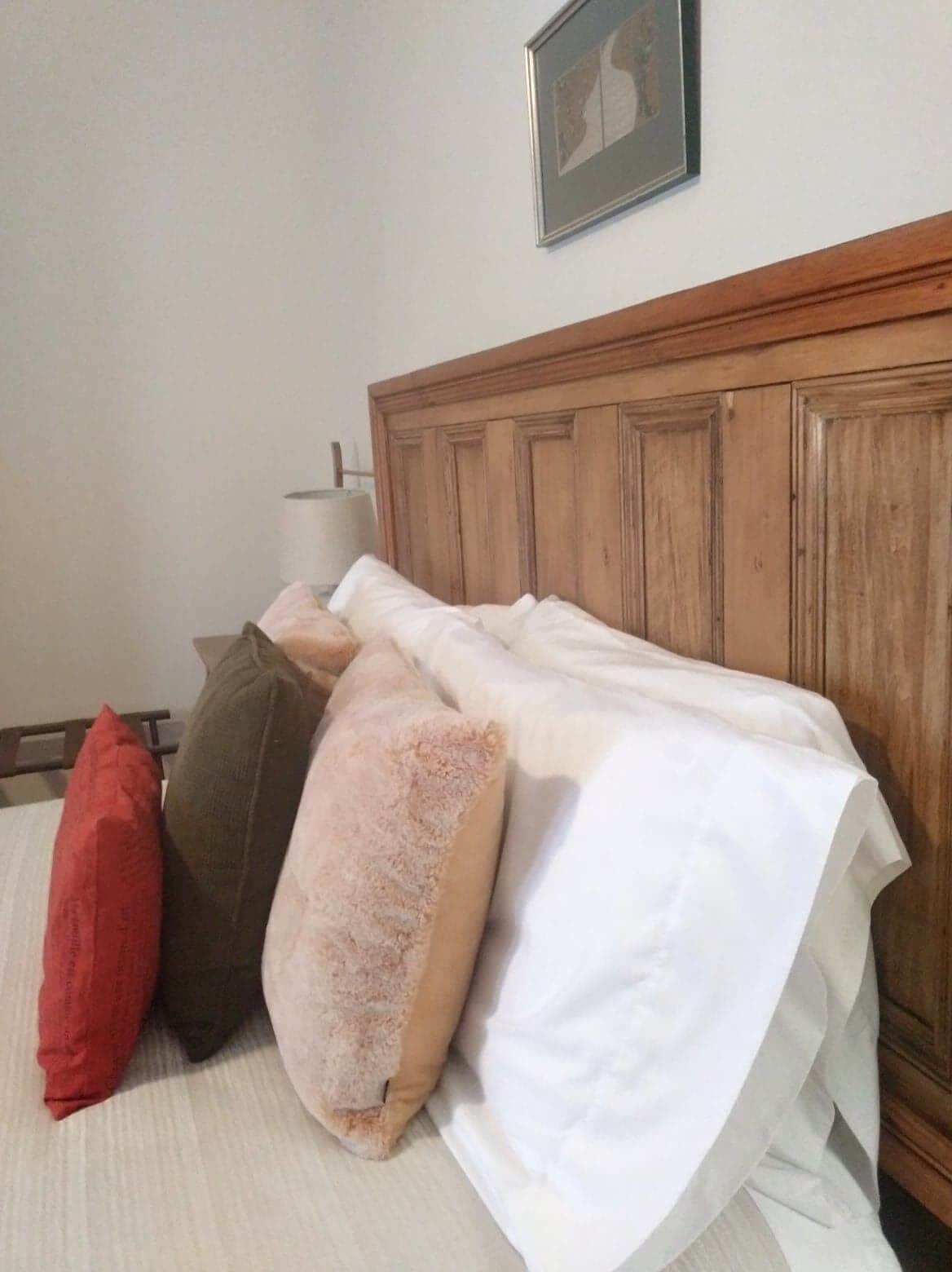 A bed with a wooden headboard, a white comforter, and three pillows in different colors.