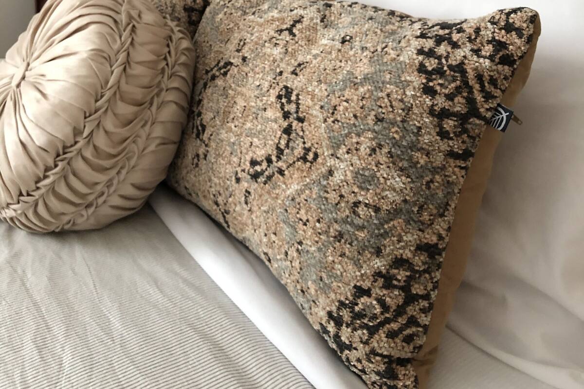 Una cama con cabecera de madera, dos almohadas decorativas, una lámpara y una mesita de noche.