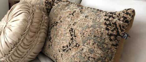 Una cama con cabecera de madera, dos almohadas decorativas, una lámpara y una mesita de noche.