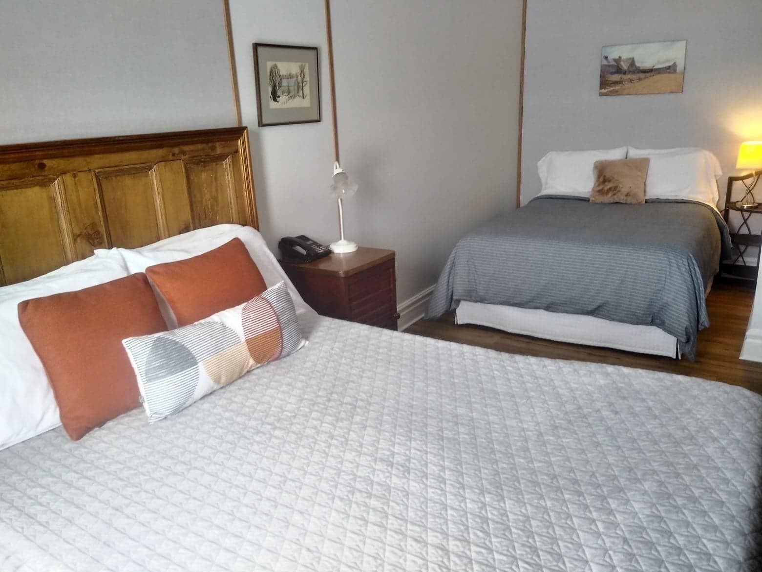 A hotel room with two beds, a wooden headboard, a bedside table with a lamp, and a nightstand with a phone.