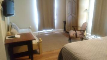 Une chambre d’hôtel équipée d’un lit, d’un bureau, d’une chaise, d’une armoire et d’un téléviseur fixé au mur.