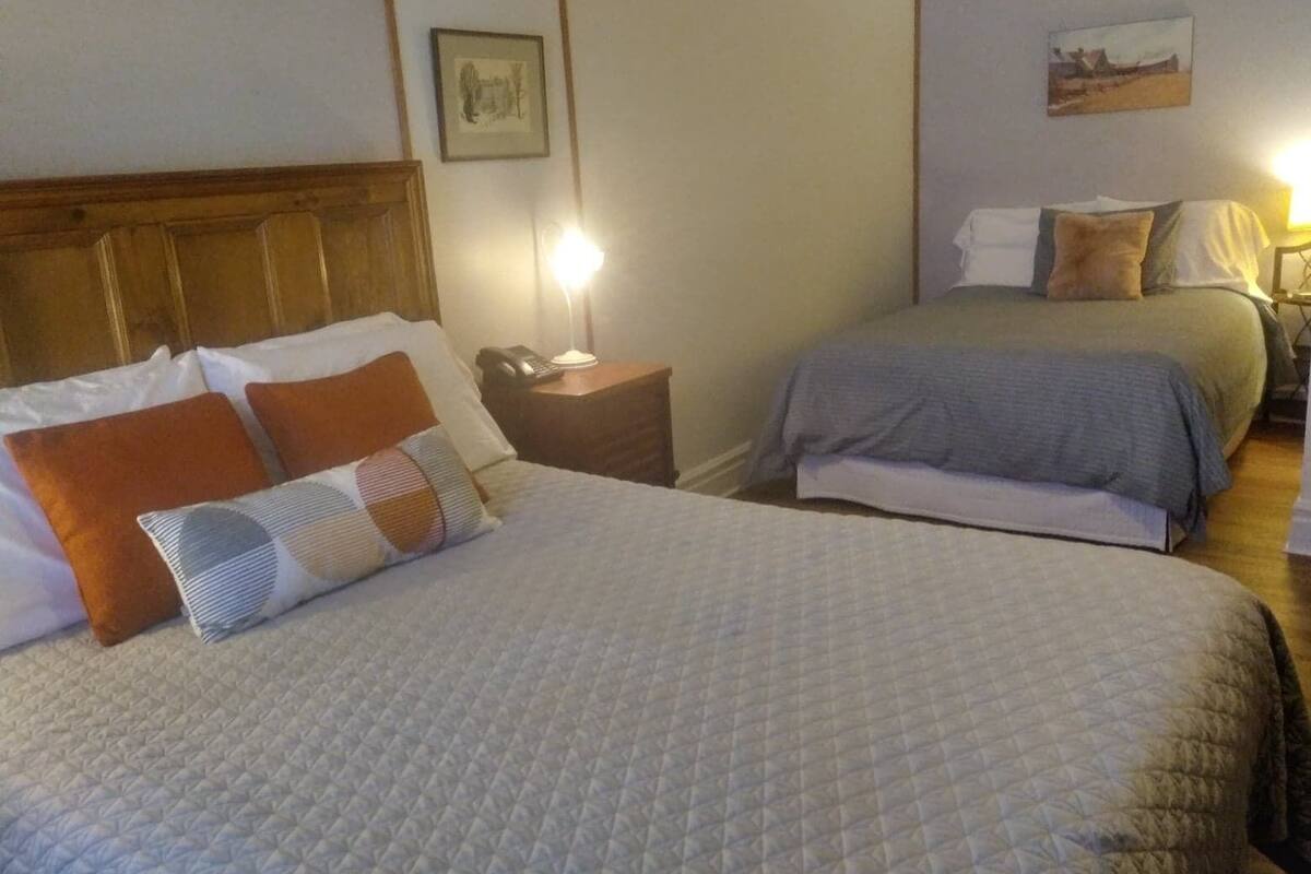 Habitación de hotel con dos camas, cada una con un estilo diferente de ropa de cama. Hay mesitas de noche con lámparas y teléfono.