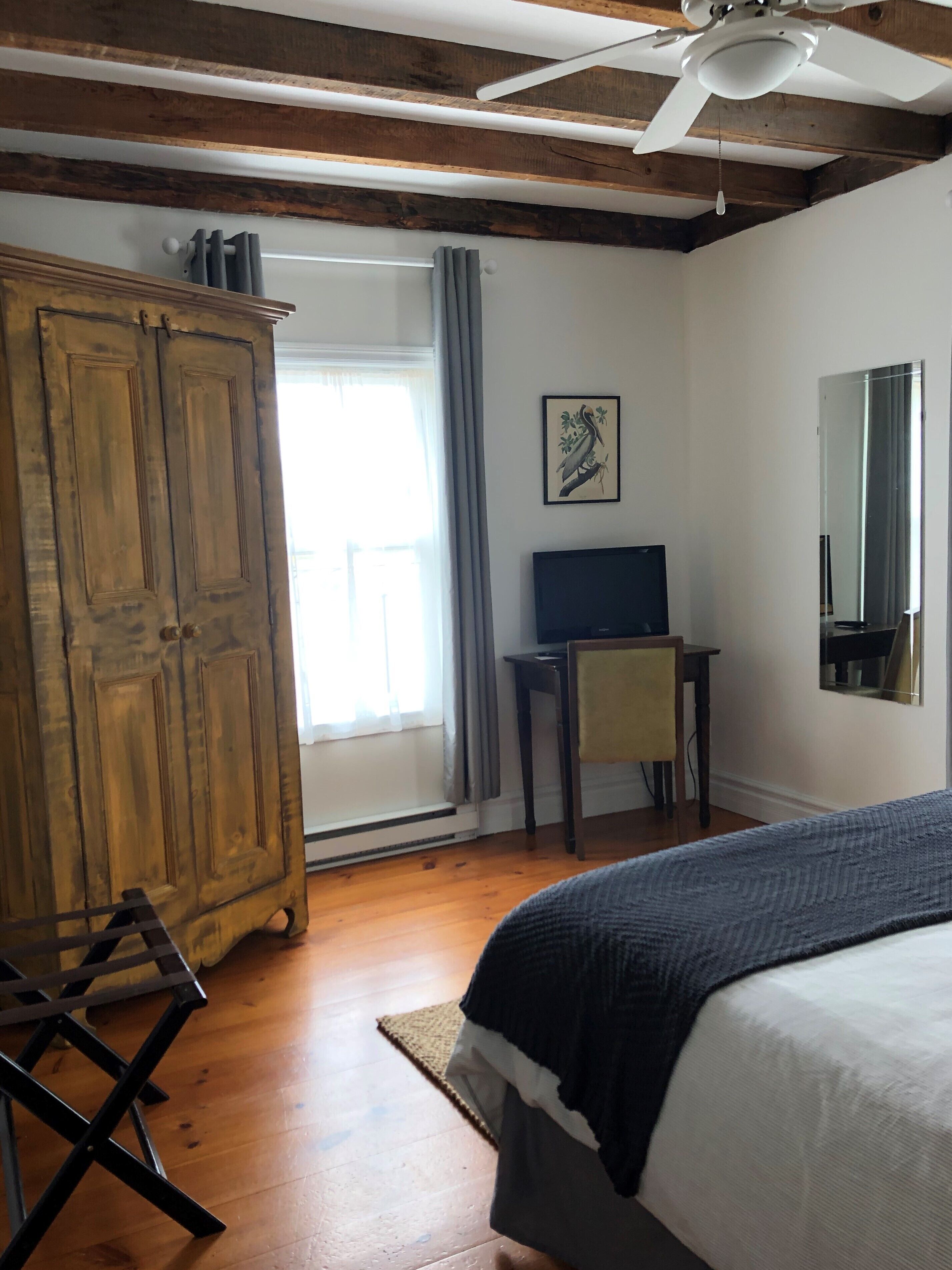 Een slaapkamer met een bed, een bureau, een stoel, een kledingkast en een plafondventilator.