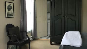 Un dormitorio con cama, una silla, un armario y una puerta que da al baño.