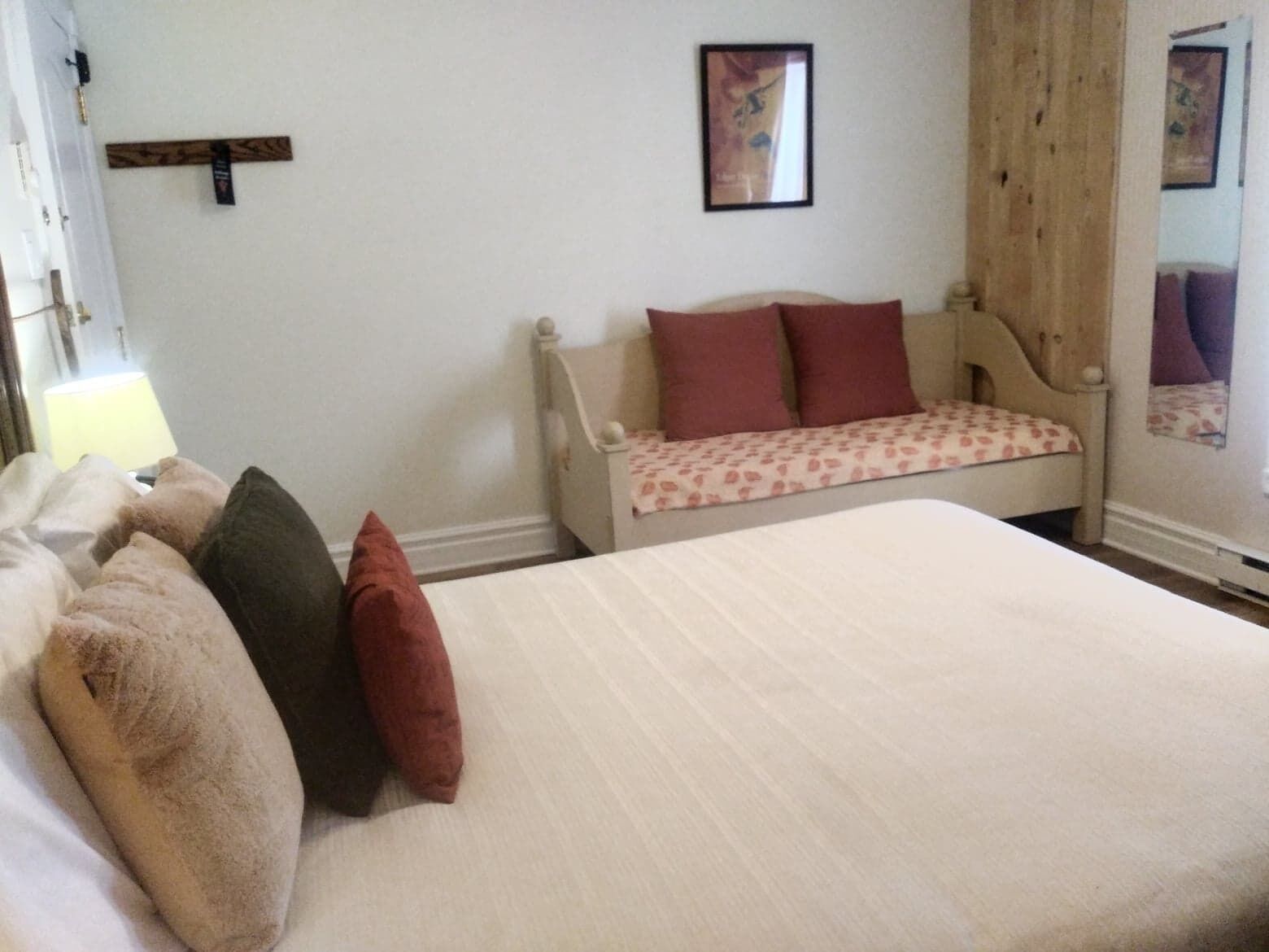 Un dormitorio con una cama, cabecera de madera, mesita de noche, lámpara y espejo.