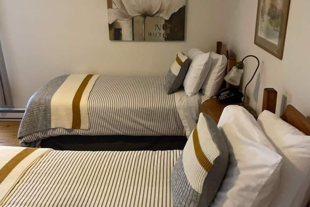 Habitación de hotel con dos camas, ropa de cama a rayas, un cuadro enmarcado sobre las camas y una mesita de noche con una lámpara.