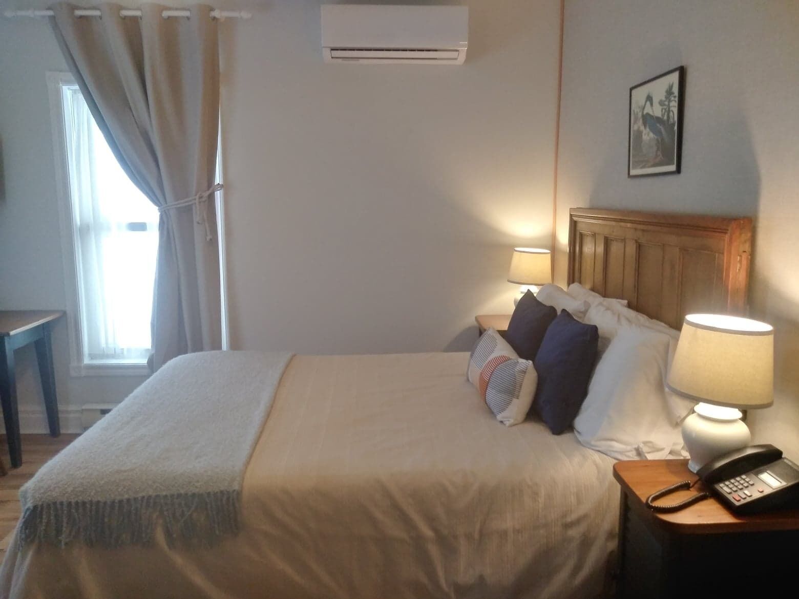 Une chambre d’hôtel avec un lit, des lampes de chevet, un téléphone et un tableau au mur.