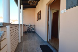 A narrow hallway with a wooden floor, a black mat at the entrance, and a rustic cart with a wheel and a bucket. - Apartment Kuftic - Relax Zone (Rovinj)