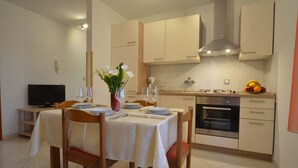 A modern kitchen with a dining area set for four, including a TV, a vase with flowers, and a fruit bowl. - Apartment Kuftic - Relax Zone (Rovinj)