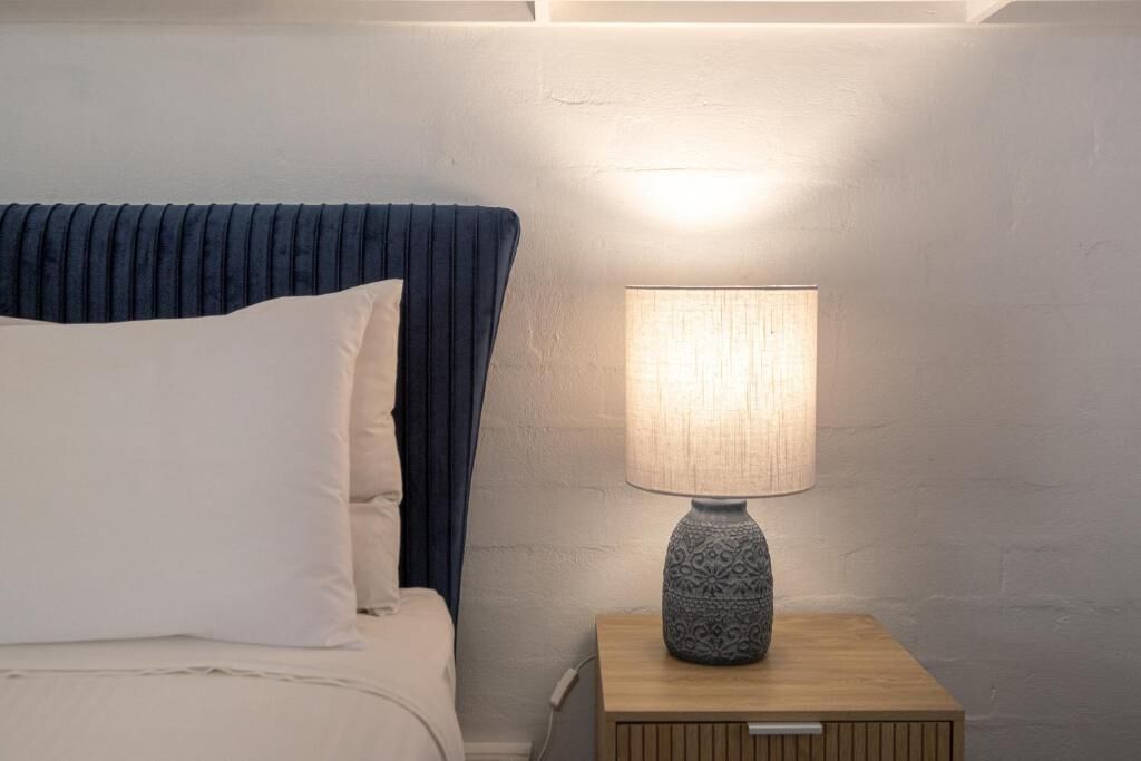 A bed with a blue headboard and white pillows, a bedside table with a lamp, and a wall with a textured finish.