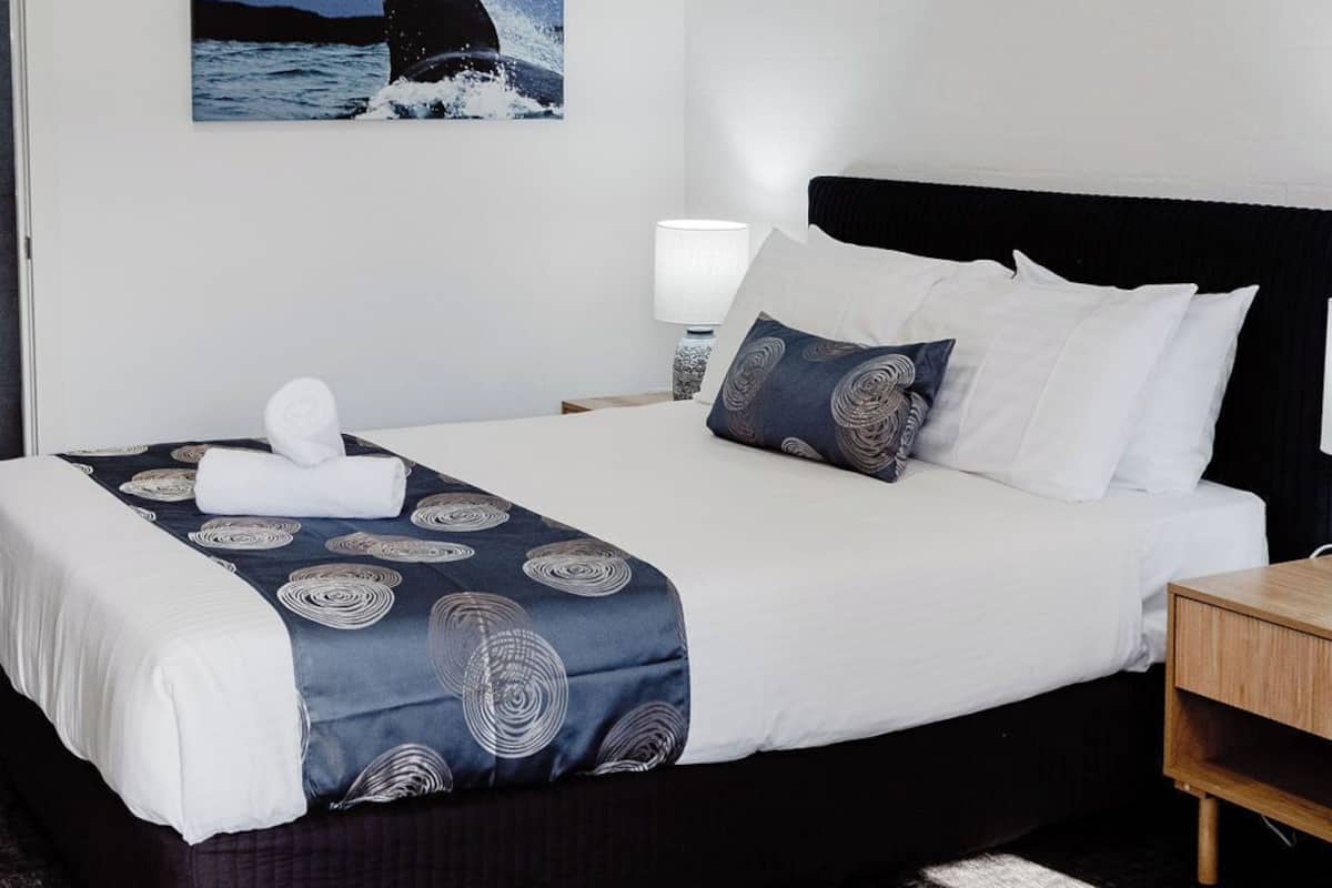 A hotel room with a bed, a nightstand, a lamp, and a wall-mounted picture of a whale.
