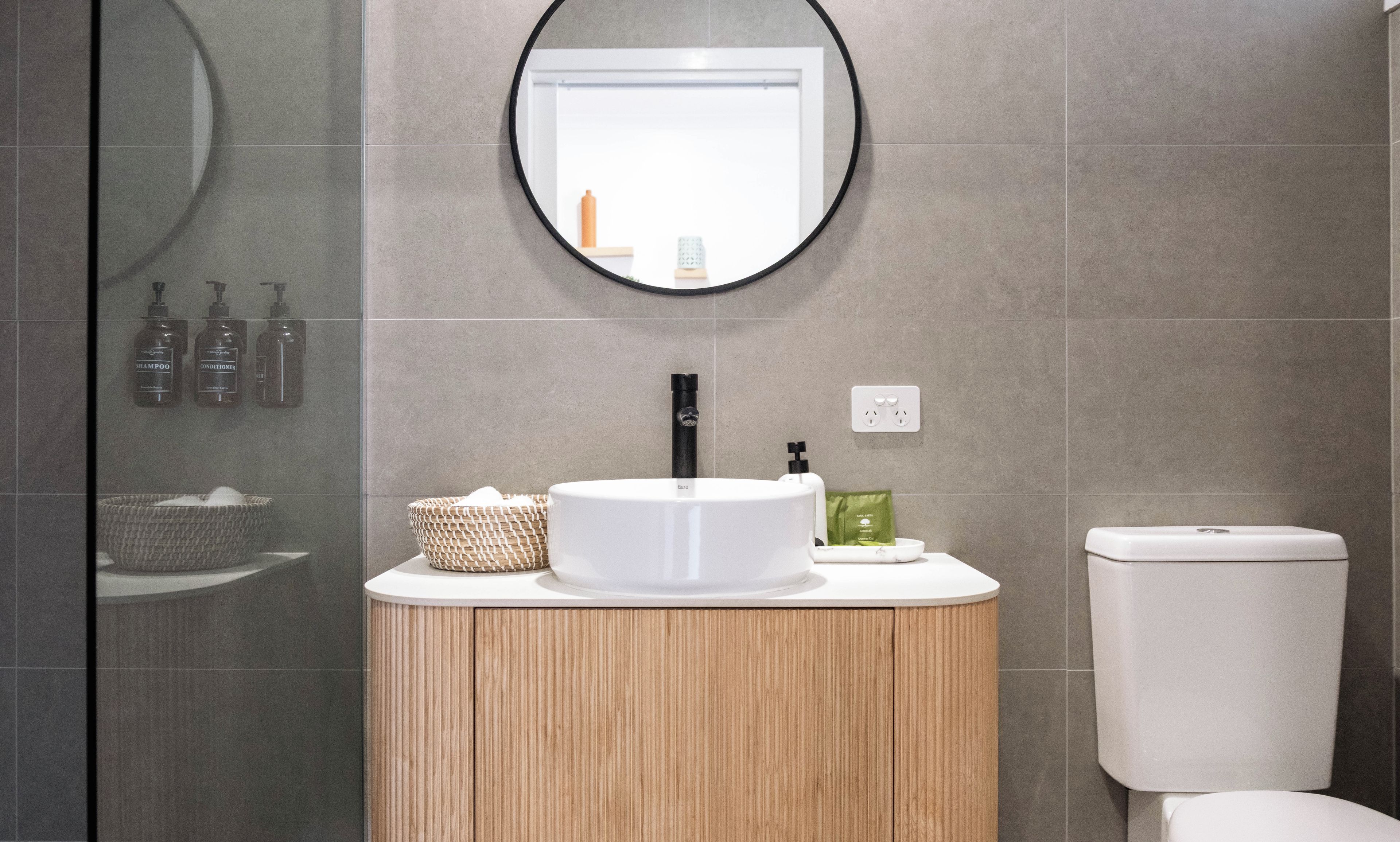 A bathroom with a round mirror, a white sink, a wooden cabinet, and a toilet.