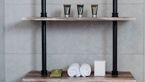 A bathroom with a wooden shelf unit, black pipes, and neatly rolled towels. - The Caledonian Inn (Port Fairy)