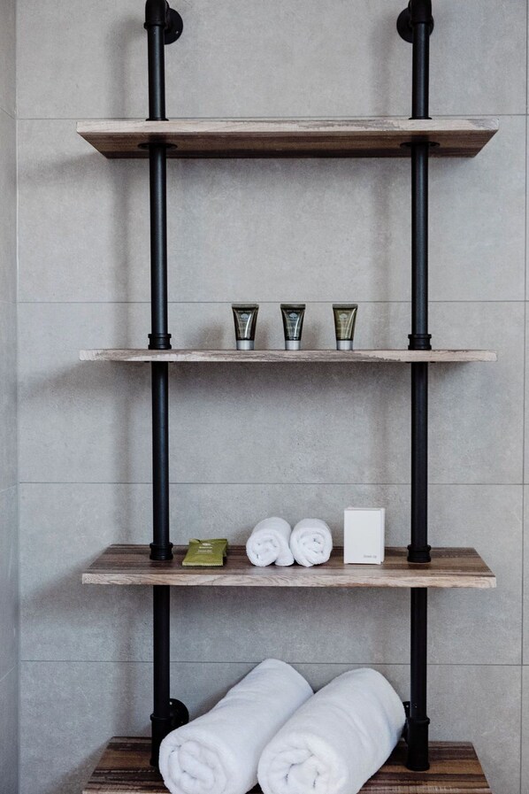 A bathroom with a wooden shelf unit, black pipes, and neatly rolled towels. - The Caledonian Inn (Port Fairy)