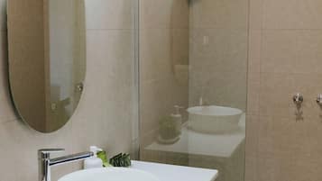 A modern bathroom with a large oval mirror, a round sink, and a glass-enclosed shower area.