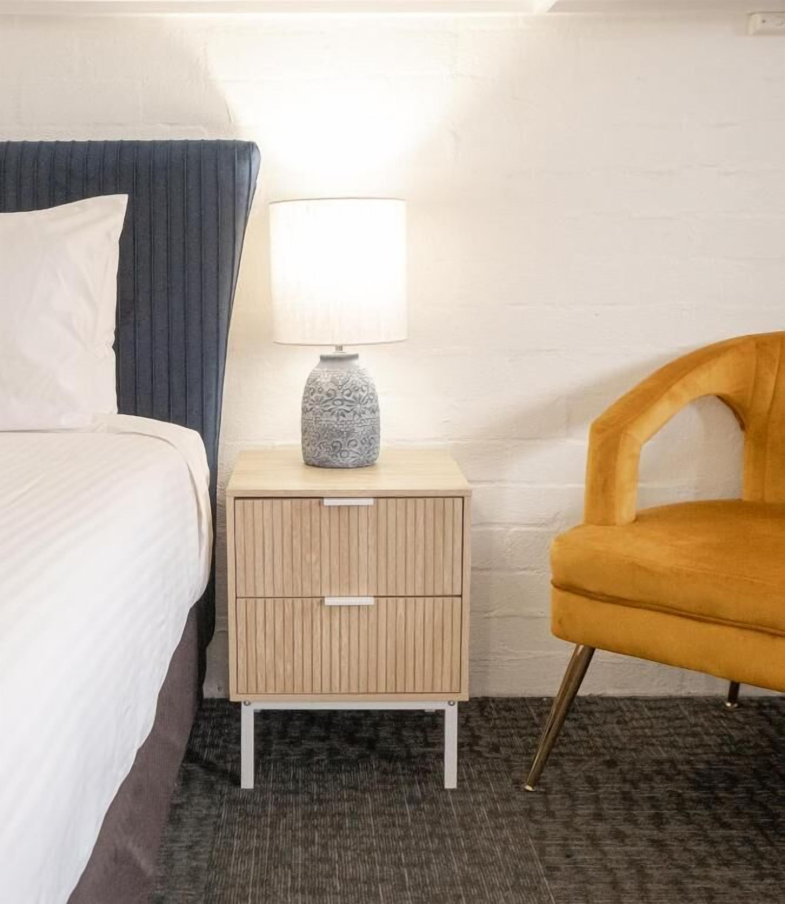 Una habitación de hotel con una cama, una mesita de noche con lámpara y una silla.