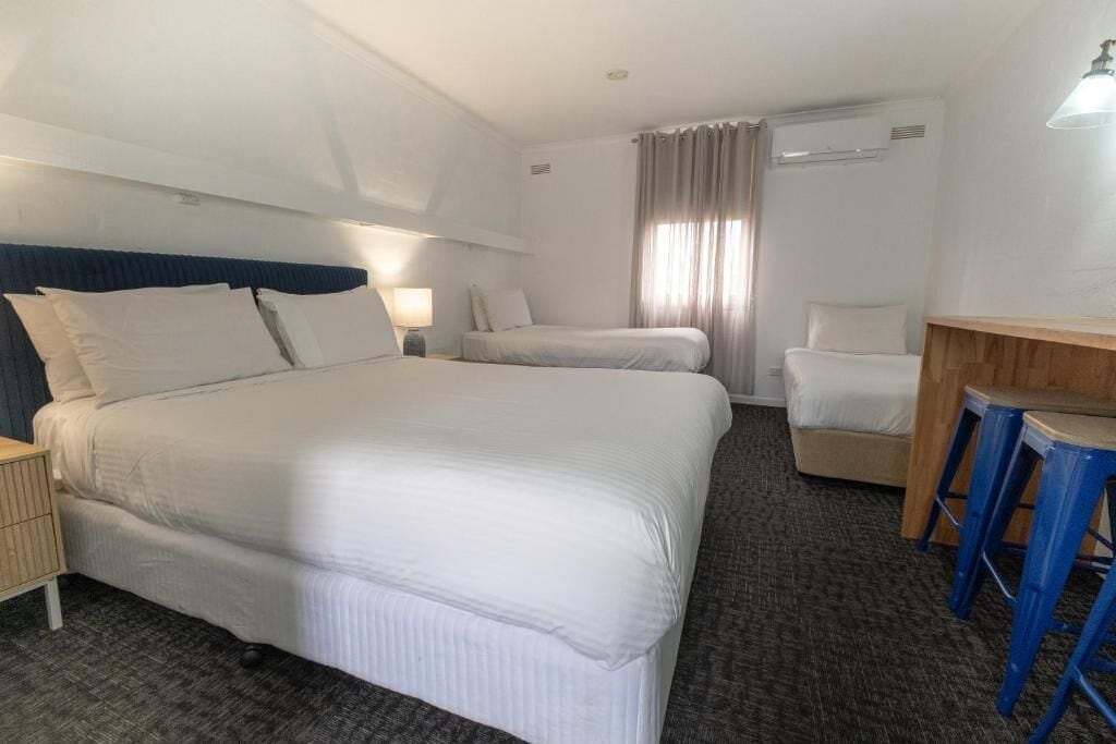 Una habitación de hotel con una cama grande, una cama más pequeña, un escritorio con taburetes y una silla.