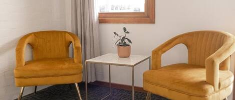 Deux chaises de couleur jaune moutarde avec des pieds en métal, une petite table et une plante en pot posée sur une table blanche.