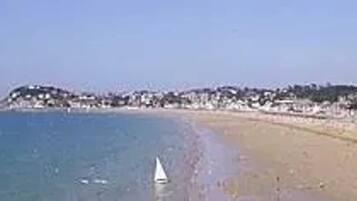 Une plage avec un voilier, un rivage sablonneux et une colline boisée en arrière-plan.