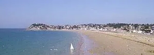 Ein Strand mit Segelboot, sandigem Ufer und einem bewaldeten Hügel im Hintergrund.