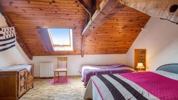 A cozy attic bedroom with a sloped ceiling, a window, a wooden dresser, a chair, and a bed with striped bedding.