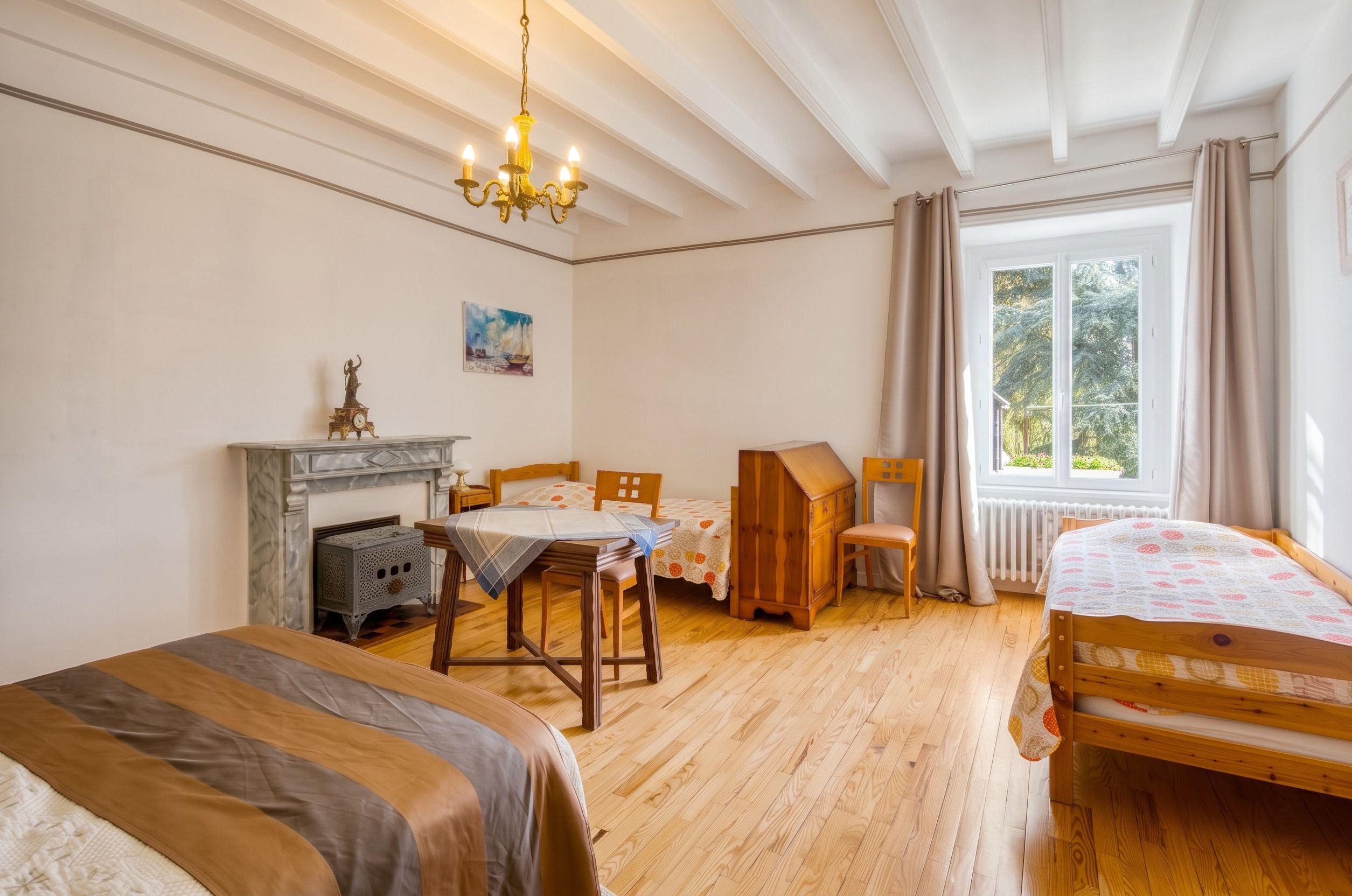 Ein Zimmer mit einem Bett, einem Schreibtisch, einem Sessel, einem Kamin und einem fensterbepflanzten Fenster.