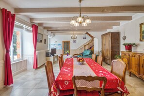 A dining area with a long table covered in a red tablecloth, wooden chairs, and a chandelier. - Homerez - House in Pordic (Pordic)
