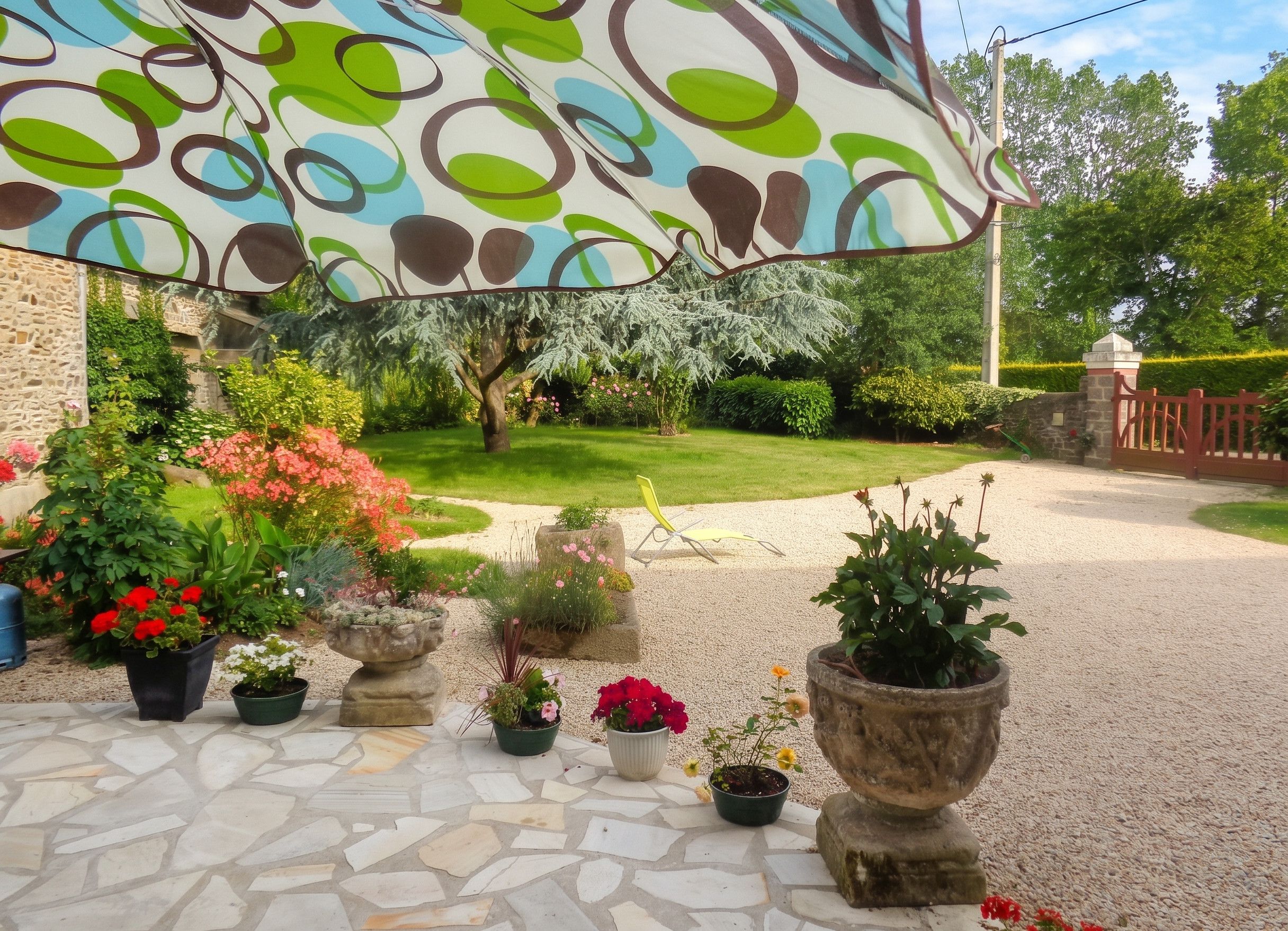 A garden patio with potted plants, a stone floor, and a decorative umbrella.