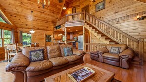 L'intérieur d'un chalet en bois, avec un canapé en cuir, une table à manger et un escalier menant à un étage supérieur.