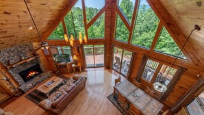 Un intérieur spacieux de chalet en bois avec une cheminée en pierre, un canapé en cuir, une table à manger en bois et de grandes fenêtres offrant une vue sur la forêt.