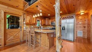 L’intérieur d’une cabane en bois comprend un espace cuisine avec un îlot central, des tabourets de bar et un réfrigérateur.