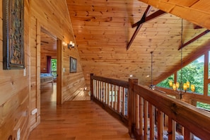 A wooden interior with a wooden floor, a balcony with a railing, and a view of greenery outside.