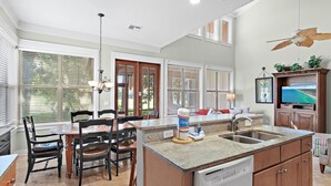 A kitchen with a central island, a dining area with chairs, a built-in dishwasher, and a large window with blinds.